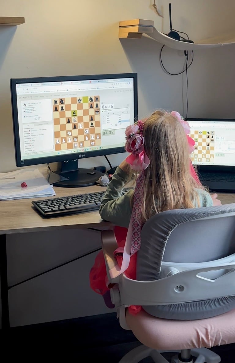 Child with pink hair bow playing chess on computer at desk with multiple monitors displaying chess game